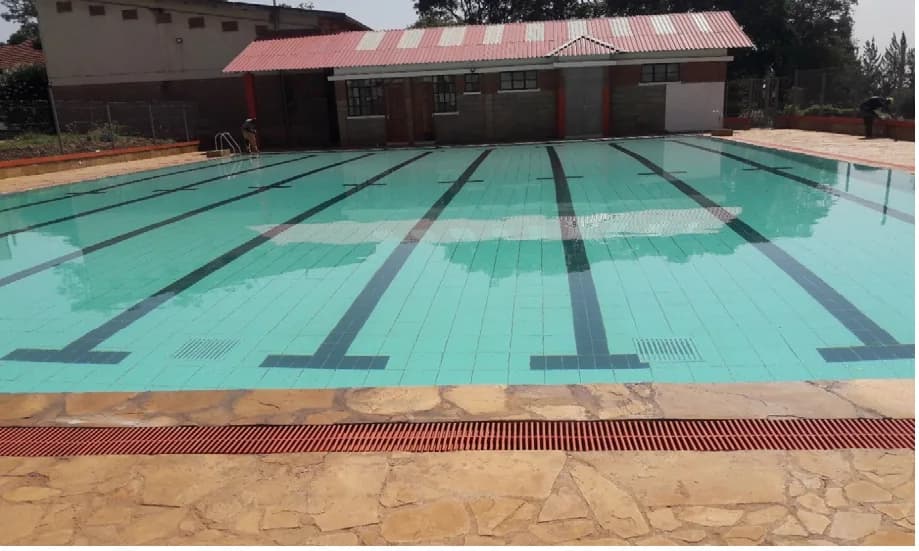 Completed outdoor swimming pool with tiled lane markings, natural stone deck, channel drainage and a changing-room block